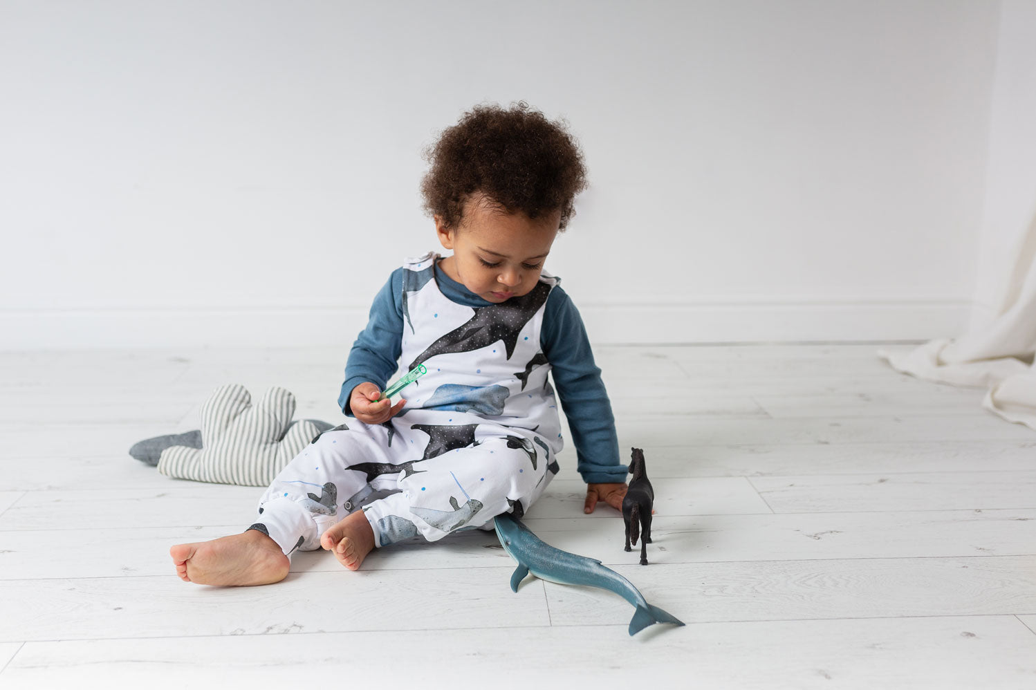 young child wearing whale print romper playing with toys in a white room ILO Clothing
