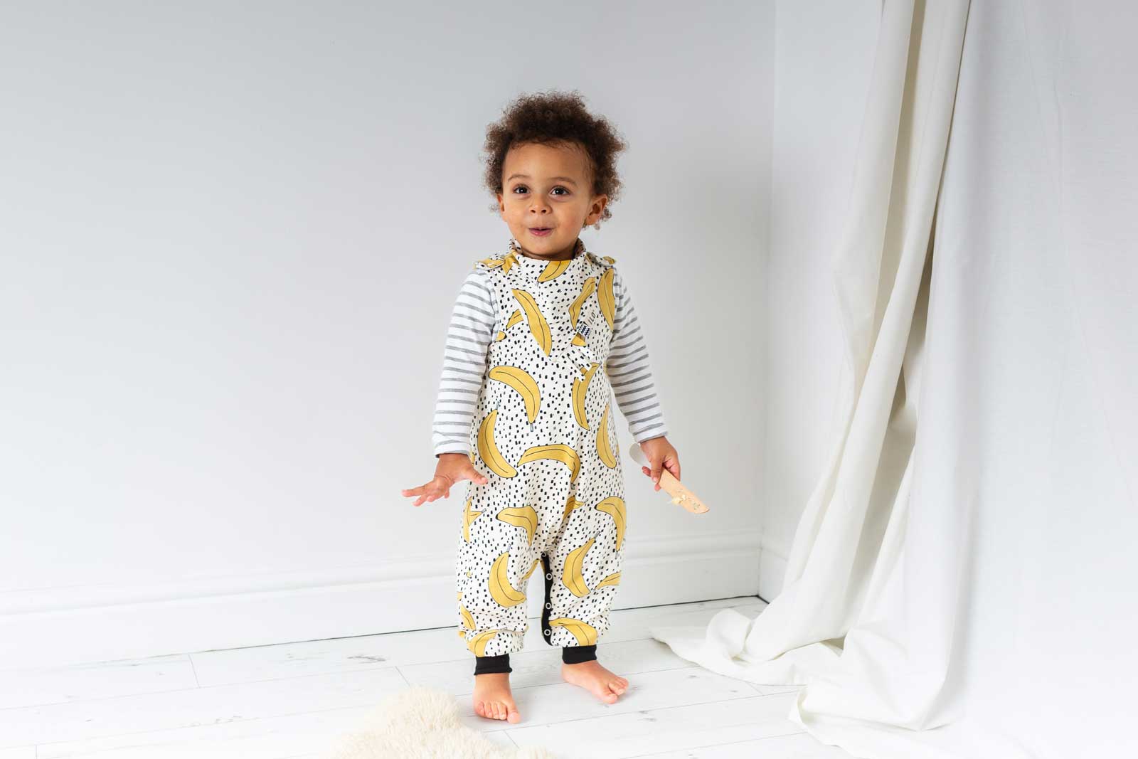 ILO Clothing young child wearing banana print romper in white room